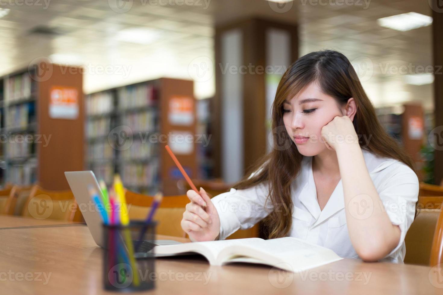 mooie Aziatische vrouwelijke student met behulp van laptop voor studie in bibliotheek foto