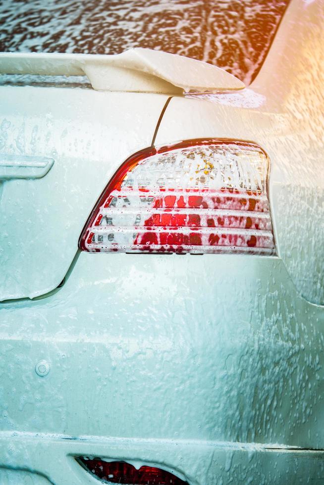 achteraanzicht van witte auto wassen met zeep. auto bedekt met wit schuim. auto zorg service bedrijfsconcept. foto