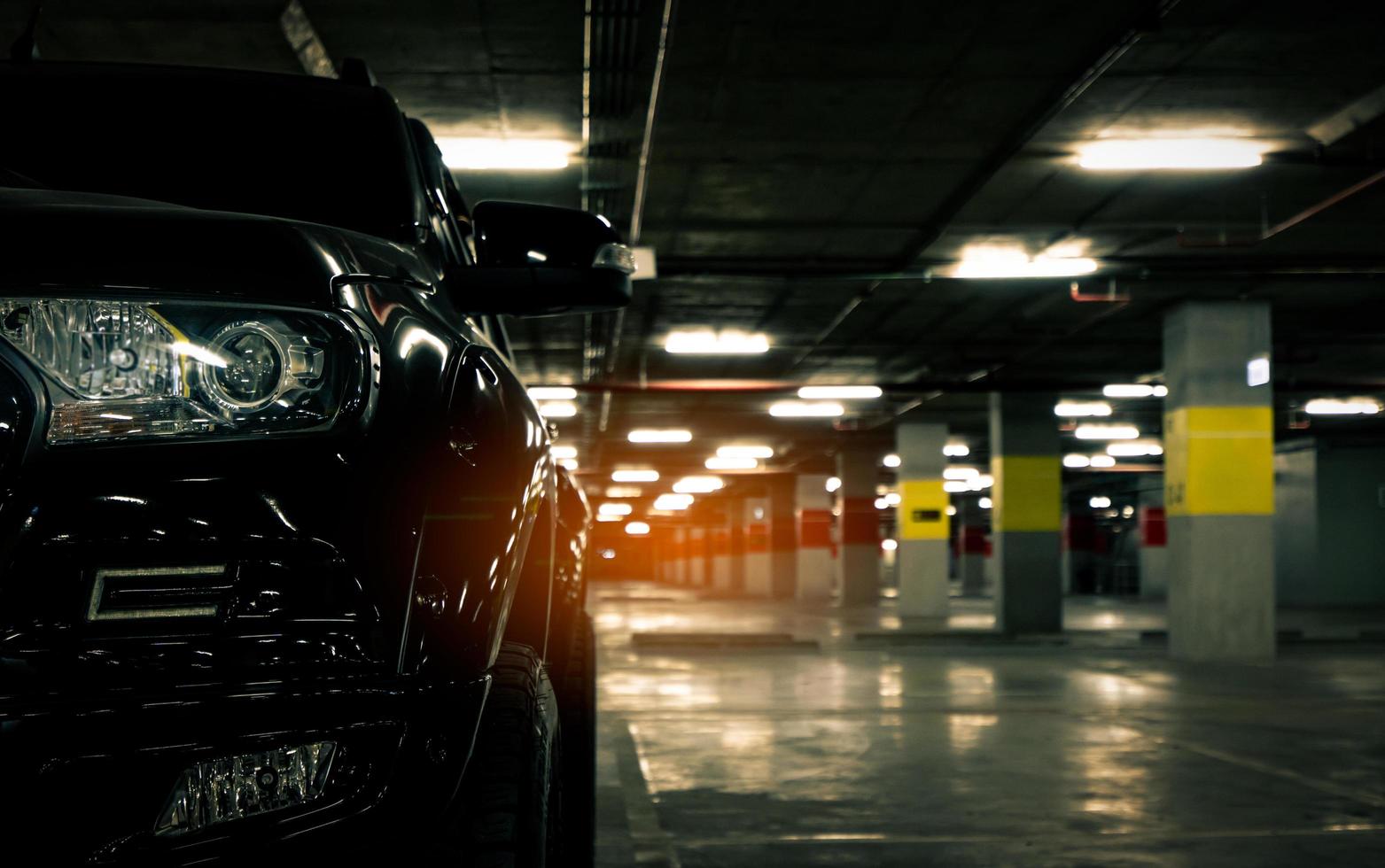 vooraanzicht van zwarte auto geparkeerd in ondergrondse parkeergarage van winkelcentrum. parkeerplaats van winkelcentrum in de avond. auto geparkeerd eenzaam 's nachts. autodief bij winkelcentrum concept. foto