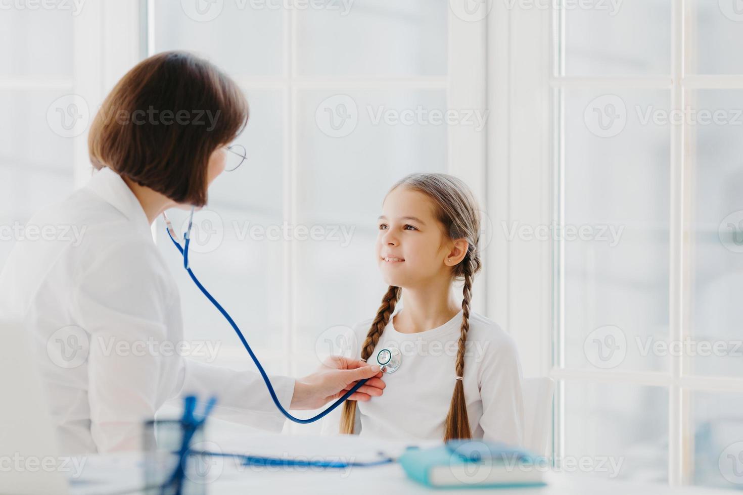 lief klein meisje luistert consult van professionele ervaren arts die haar longen luistert met een stethoscoop, komt op medische controleafspraak. concept voor kindergezondheidszorg en kliniekbezoek foto