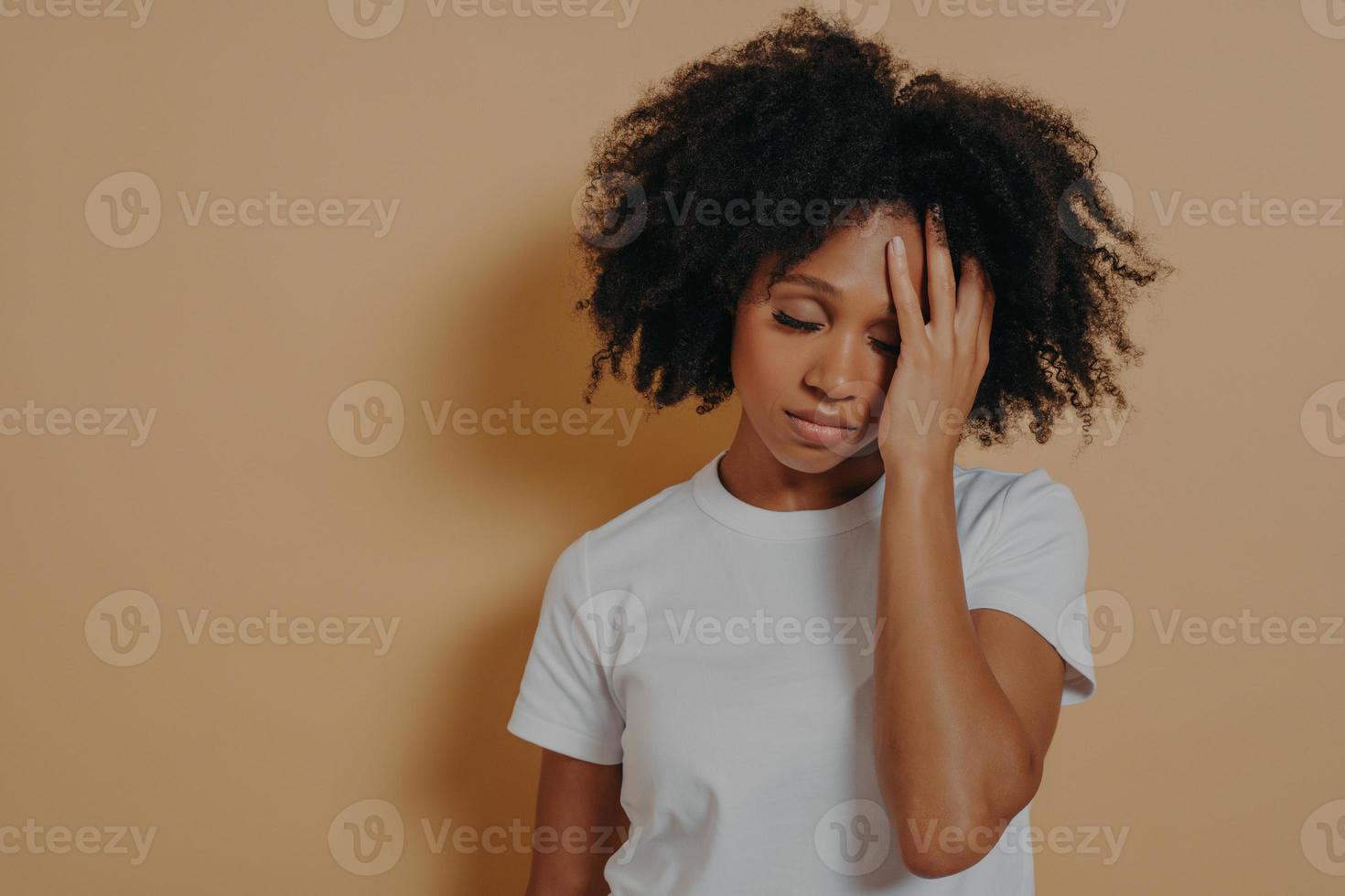overstuur vermoeide, gevilde vrouw met hoofdpijn na overwerk, geïsoleerd over beige studiomuur foto