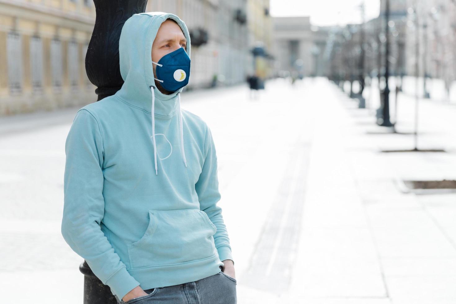 buitenopname van hipster draagt sweatshirt en ademhalingsmasker, loopt in epidemische stad, voorkomt virus, infectie en coronavirus, bang om besmet te worden. quarantaine tijd. gezondheid veiligheidsconcept foto