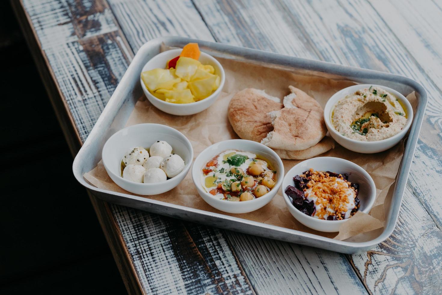 traditioneel Israëlisch keukenconcept. bovenaanzicht van smakelijke exotische gerechten geserveerd op dienblad. pitabroodje, groenten op de grill, geitenkaas, hummus op houten tafel foto