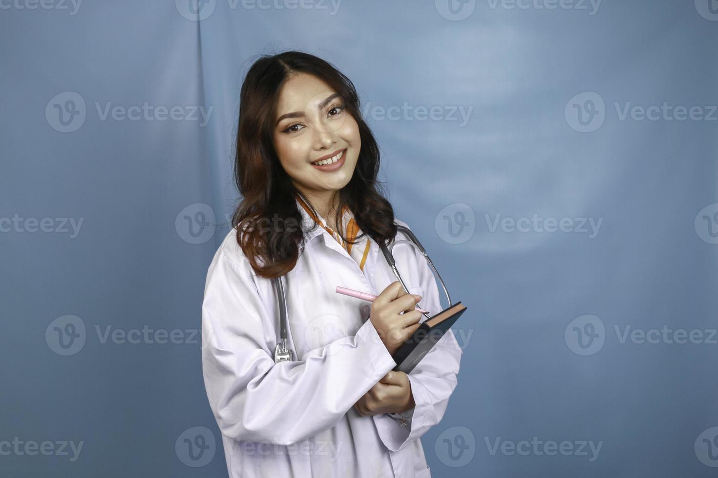 portret van een jonge Aziatische vrouwelijke arts, een medische professional lacht en houdt notities vast die over blauwe achtergrond worden geïsoleerd foto