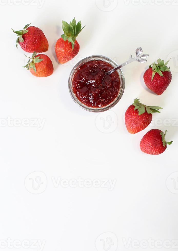 zelfgemaakte aardbeienconserven of jam in een glazen pot omgeven door verse biologische aardbeien. selectieve aandacht met witte achtergrond. foto