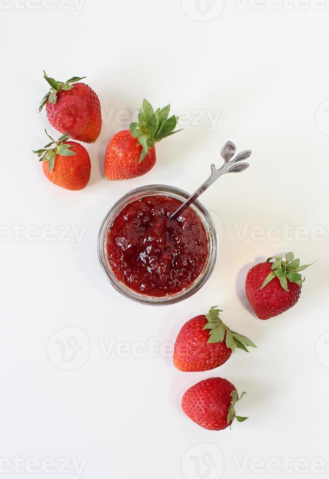 zelfgemaakte aardbeienconserven of jam in een glazen pot omgeven door verse biologische aardbeien. selectieve aandacht met witte achtergrond. foto