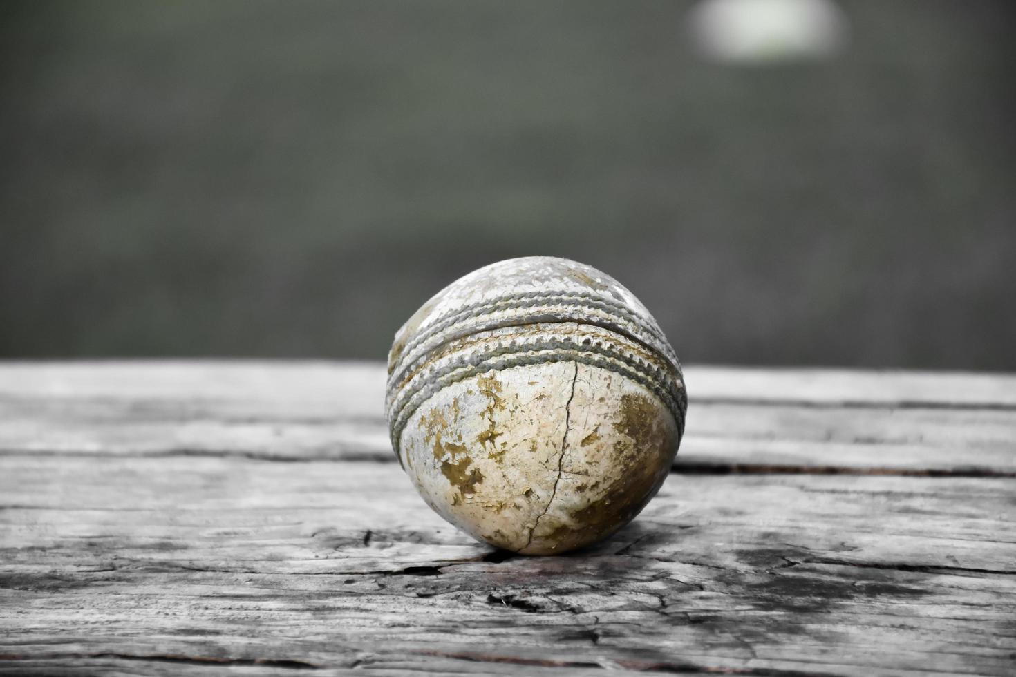 oude trainingscricket-sportuitrusting op donkere vloer, leren bal, wickets, helm en houten vleermuis, zachte en selectieve focus, traditionele cricketsportliefhebbers over de hele wereld. foto