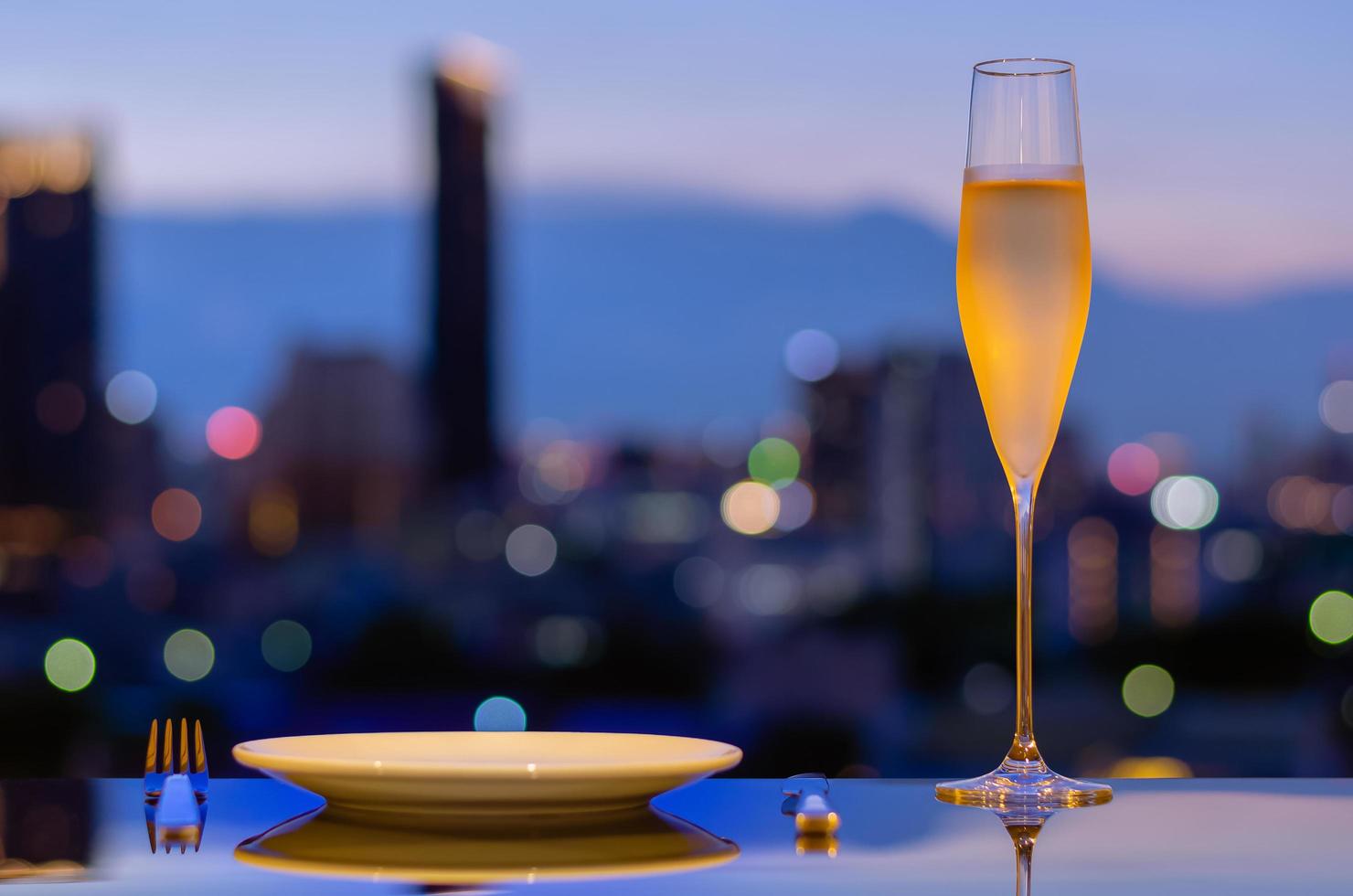 een glas met damp van koude champagne met schotel om te dineren op tafel met kleurrijke stad bokeh lichten achtergrond. foto