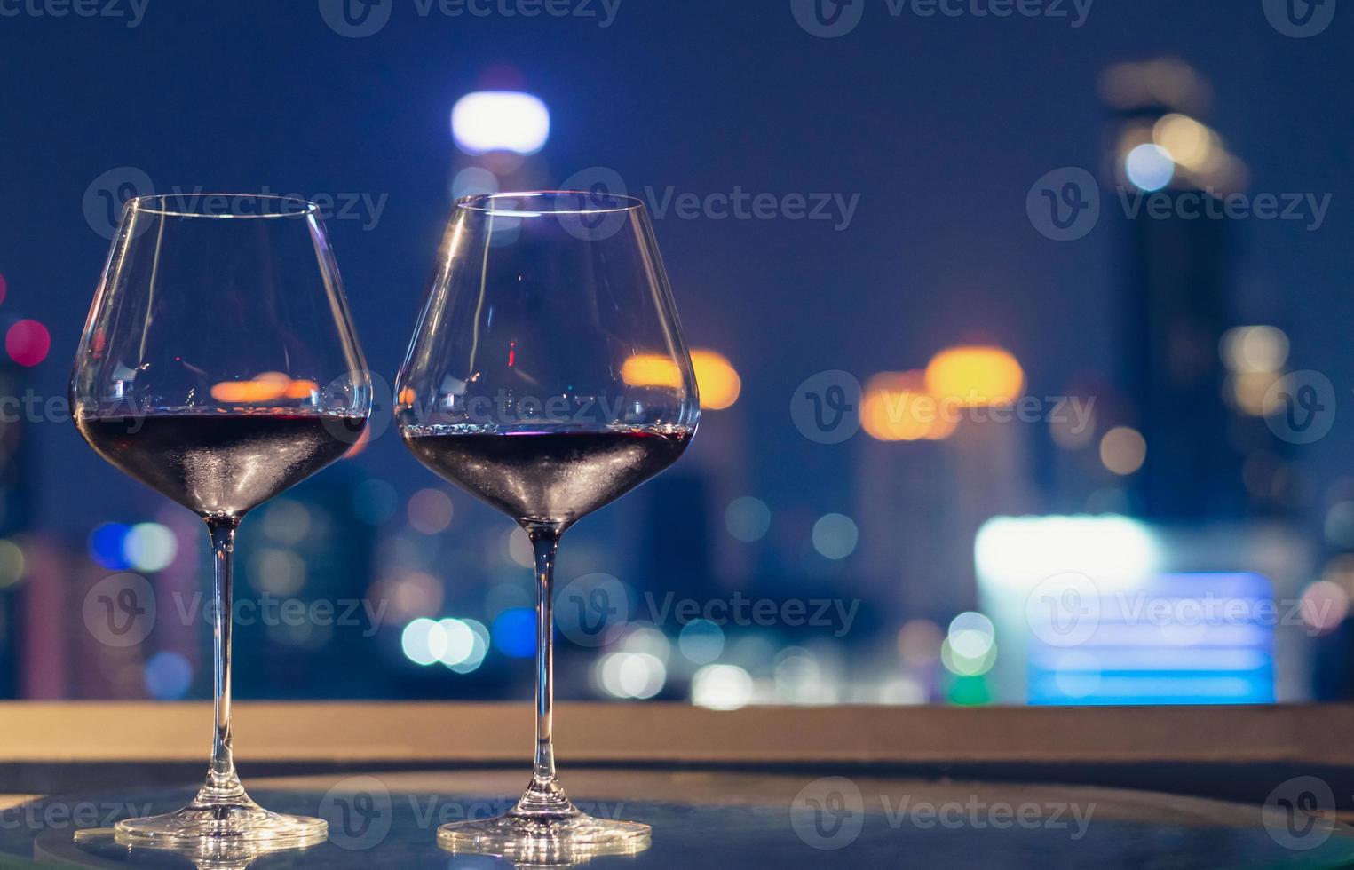 twee glazen rode wijn op tafel van bar op het dak met kleurrijke bokeh van stadslichten. foto