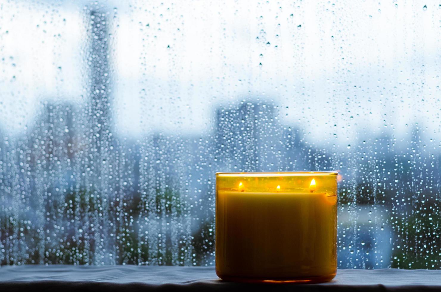 brandende aromakaars wordt bij het raam geplaatst met regendruppels in het moessonseizoen. zen en ontspannen concept. foto