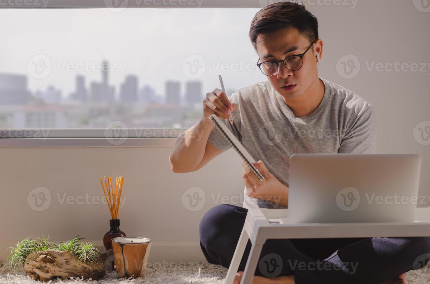 Aziatische man in vrijetijdskleding zittend en werkend op laptop in de kamer foto