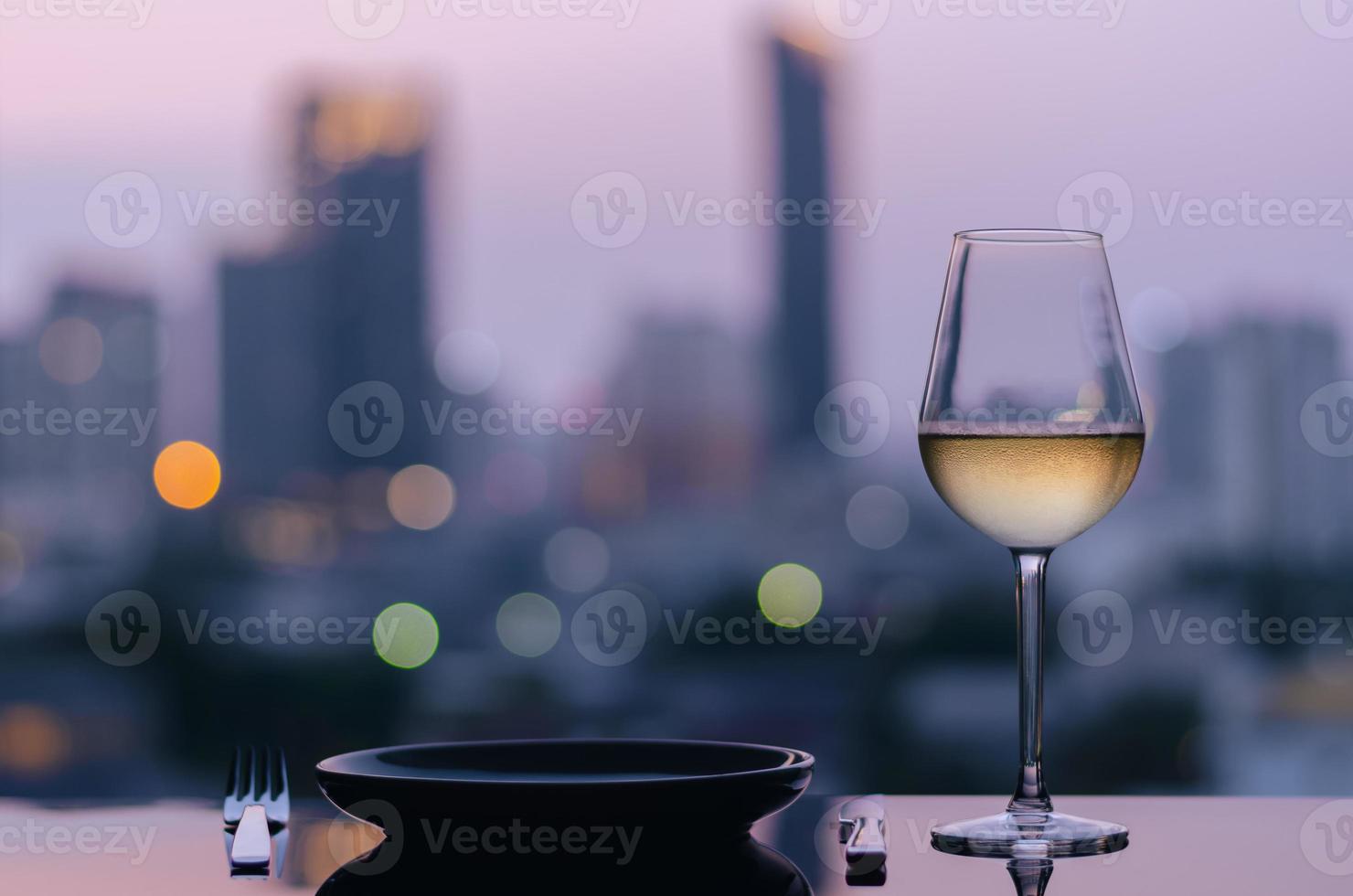 een glas witte wijn met schotel om te dineren op tafel met kleurrijke stad bokeh lichten achtergrond. foto