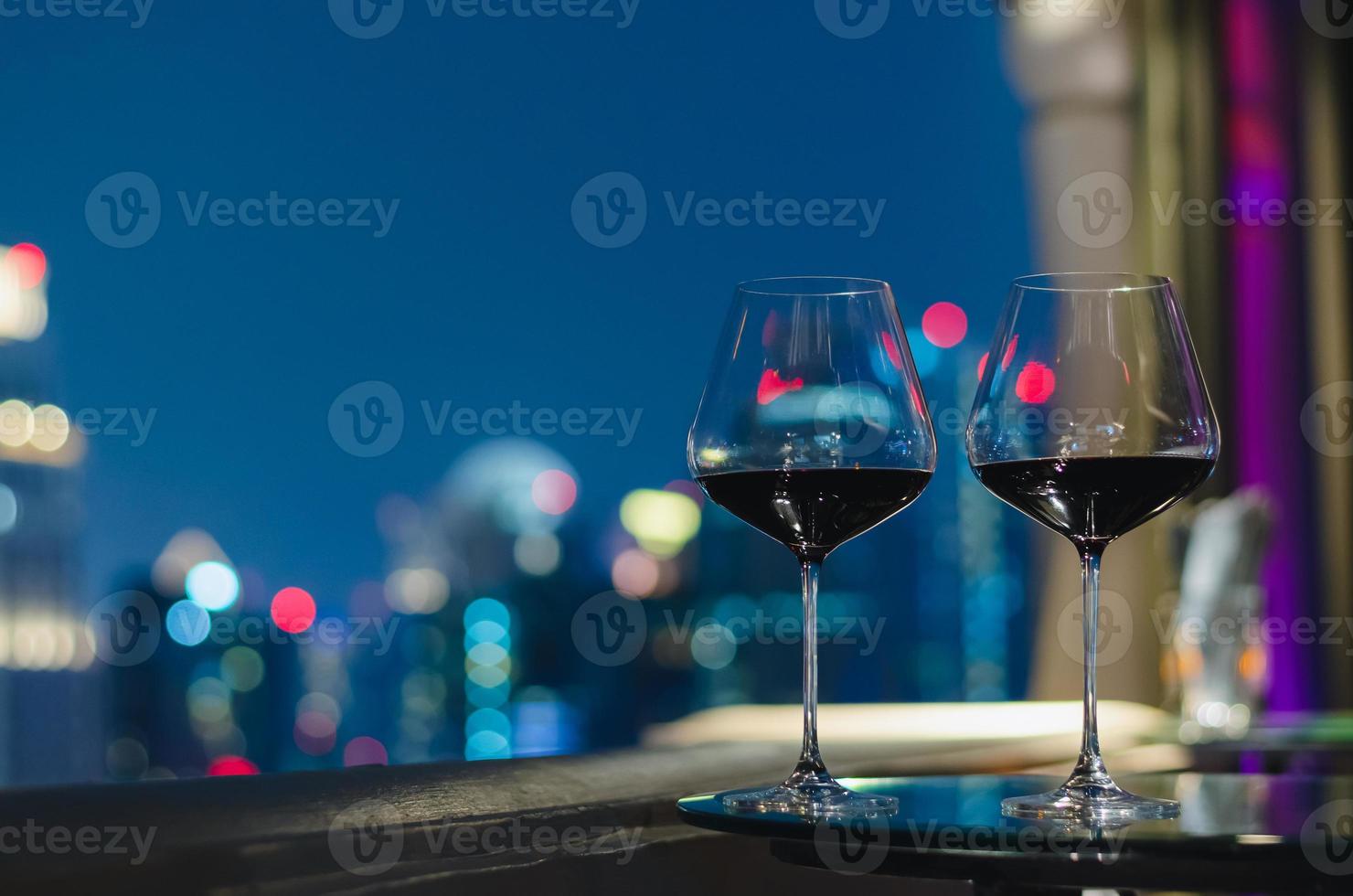 twee glazen rode wijn op tafel van bar op het dak met kleurrijke bokeh van stadslichten. foto