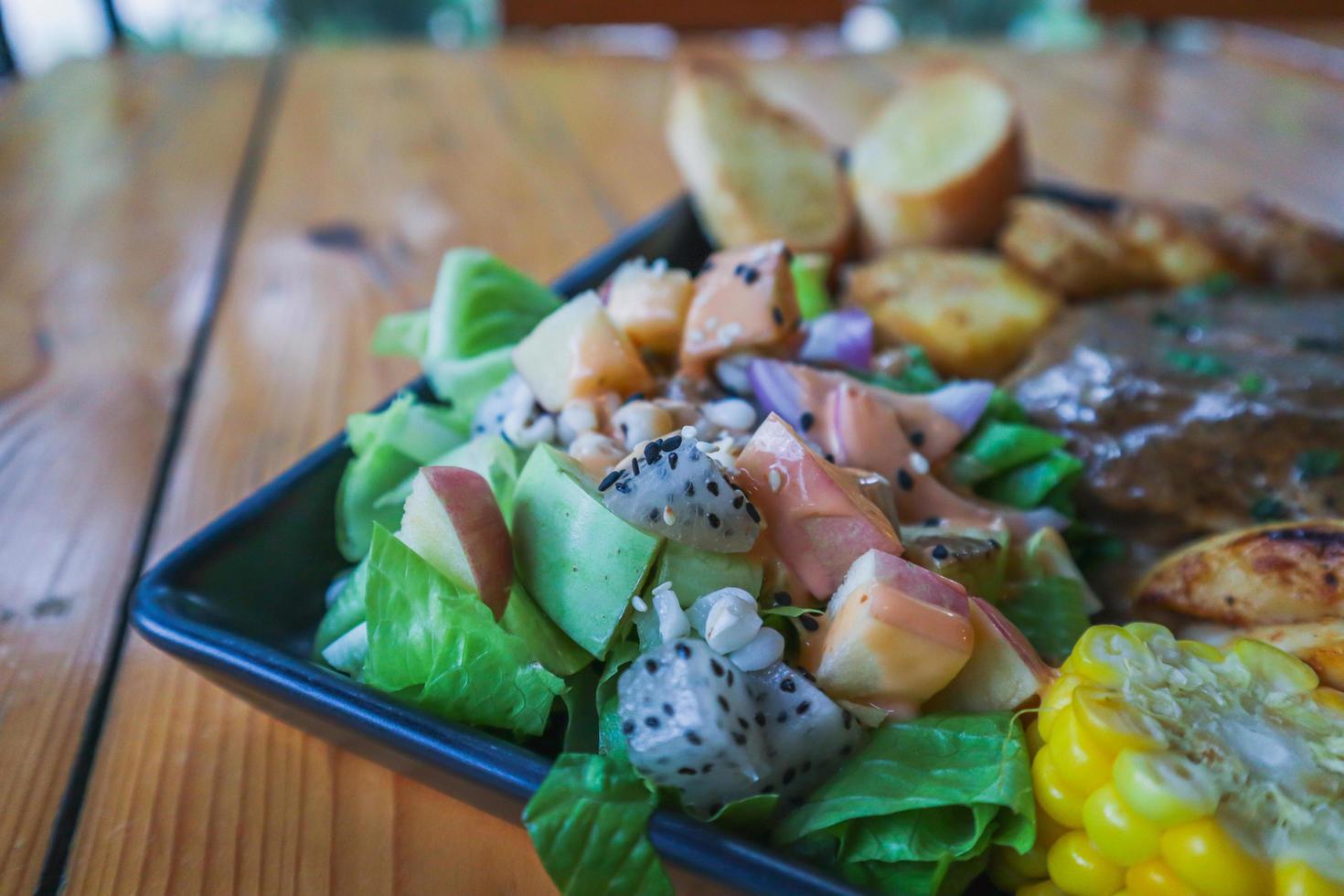 gegrilde biefstuk met jus wordt geserveerd met een groente- en fruitsalade in een zwarte keramische plaat op de eettafel om de biefstuk voor te bereiden op een feestelijk diner. foto