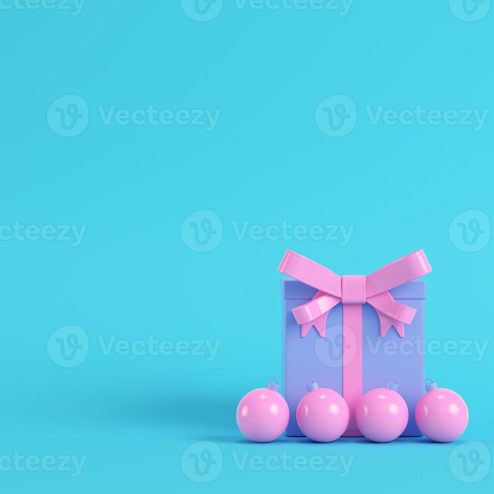 roze geschenkdoos met strik en kerstbal op felblauwe achtergrond in pastelkleuren foto