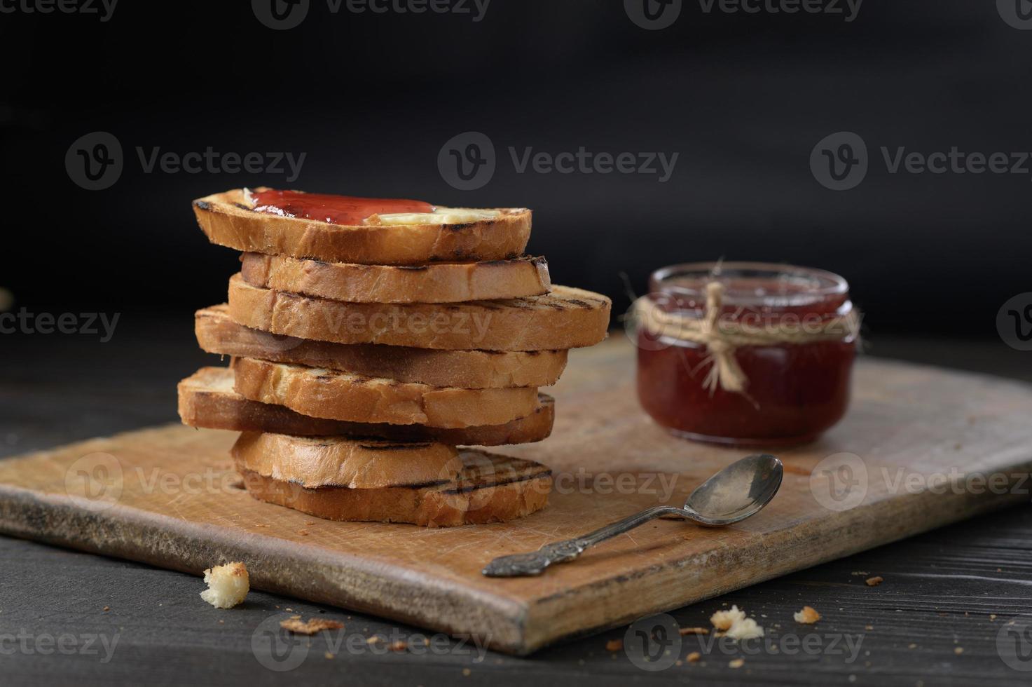 toastbrood met zelfgemaakte aardbeienjam en op rustieke tafel met boter voor ontbijt of brunch. foto