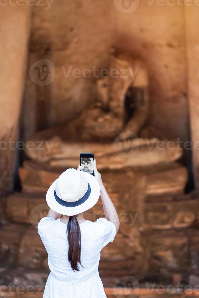 gelukkige toeristische vrouw in witte jurk die foto maakt met mobiele smartphone, tijdens een bezoek aan de wat chaiwatthanaram-tempel in het historische park van Ayutthaya, zomer, solo, Azië en Thailand reisconcept