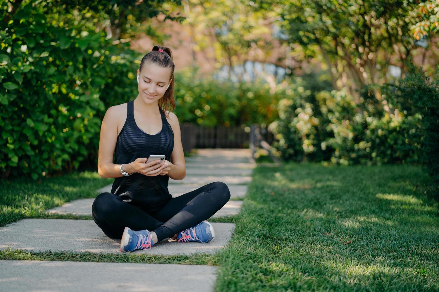 sportieve vrouw heeft pauze voor verfrissing controleert berichten en notificaties deelt inhoud over fitness buiten gekleed in actieve kleding leidt gezonde levensstijl ontspant na actieve cardiotraining foto