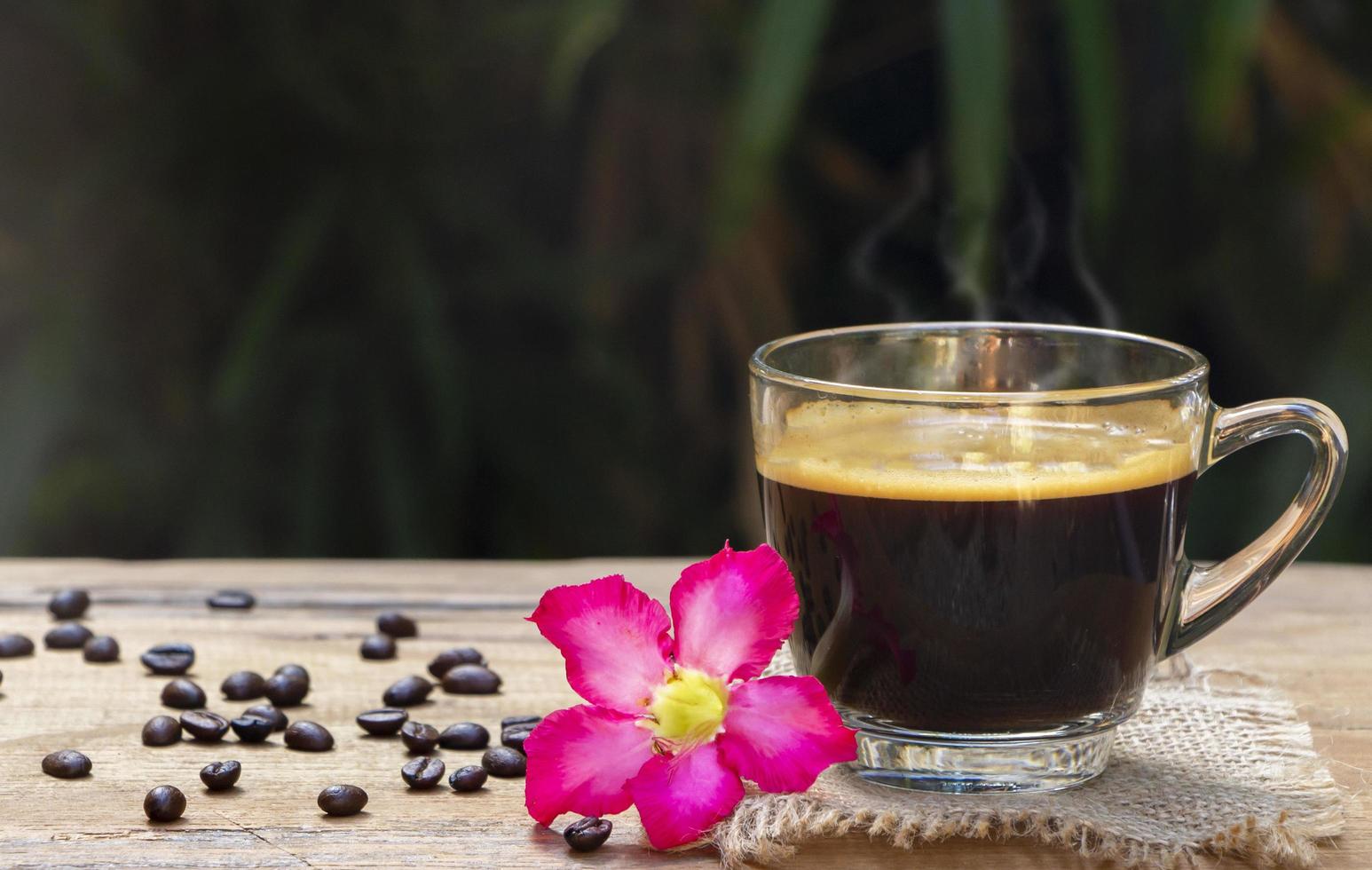 kopje hete zwarte americano-koffie met mooie rook boven een kopje op een zak en houten tafel op een natuurlijke achtergrond. goedemorgen met een verfrissingsdrankconcept foto