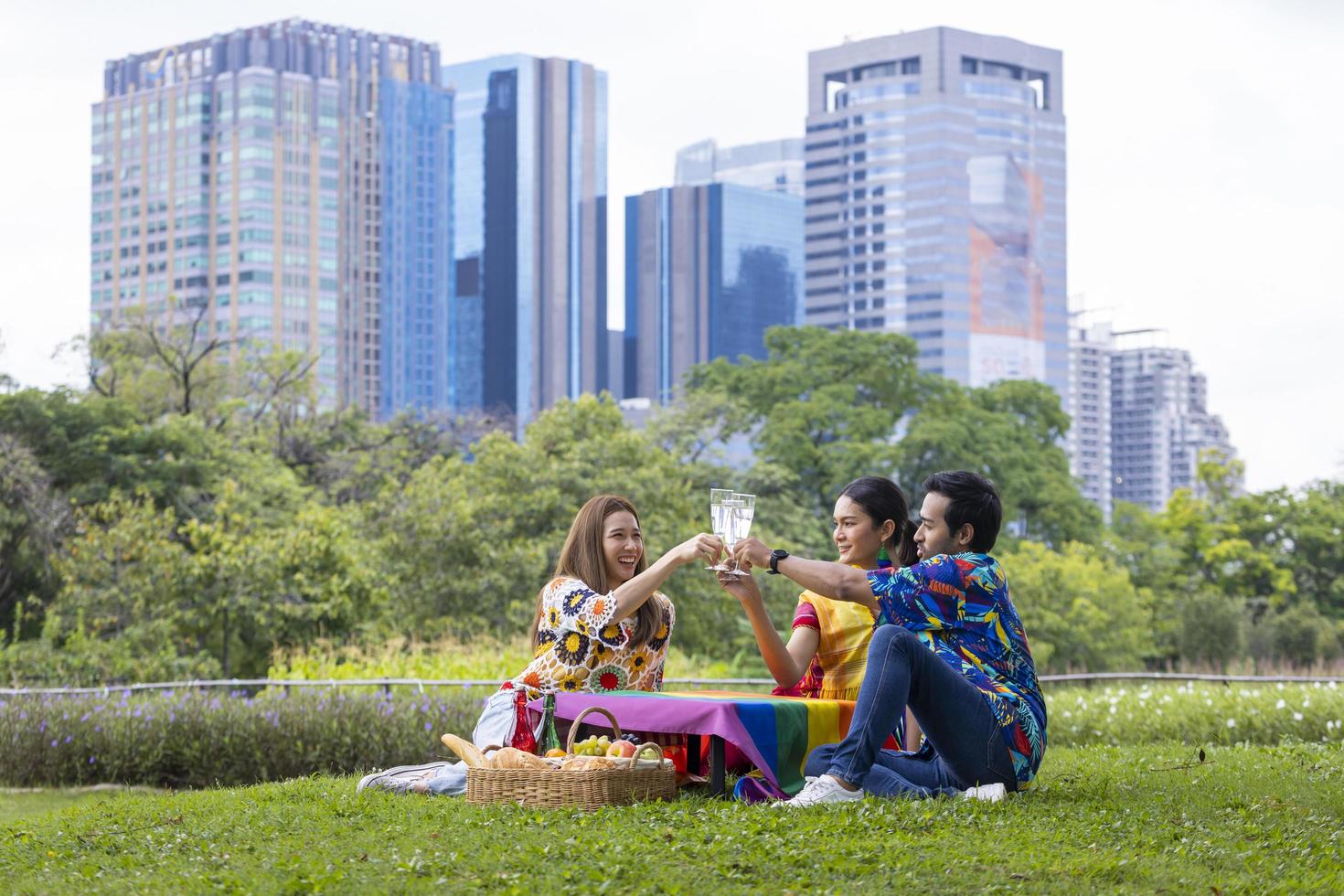 groep transgender en homoseksuele mensen juicht toe en viert lgbtq-trotsmaand in kleurrijke jurk en regenboogvlag tijdens een picknick in het park foto