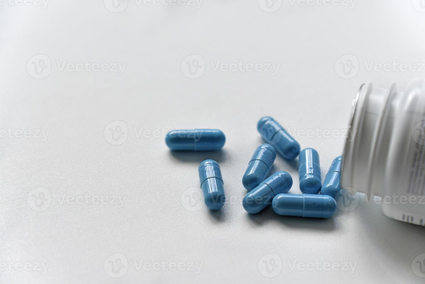 blauwe capsules uit een witte pillenpot op een witte achtergrond. foto