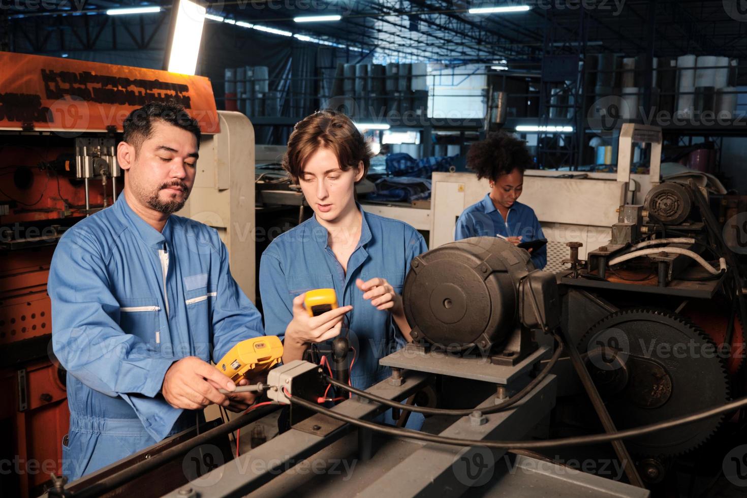 Aziatische mannelijke en blanke vrouwelijke ingenieursarbeiders in veiligheidsuniformen werken door de spanningsstroom van machines te inspecteren, te controleren en te onderhouden in de productiefabriek, elektrische systeemserviceberoepen. foto