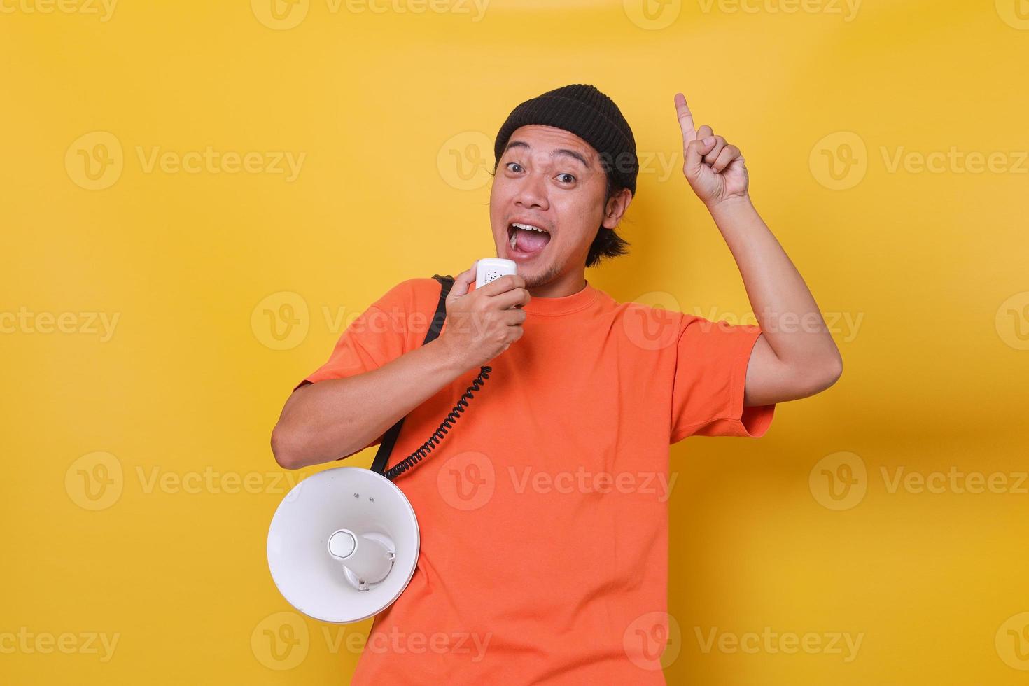 Aziatische jonge man in casual stijl met behulp van megafoon en wijzende vinger geïsoleerd op gele achtergrond. foto