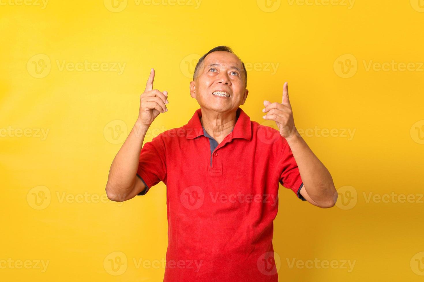 Aziatische senior man draagt rood t-shirt kijkt omhoog en wijst vingers omhoog geïsoleerd over gele achtergrond. foto