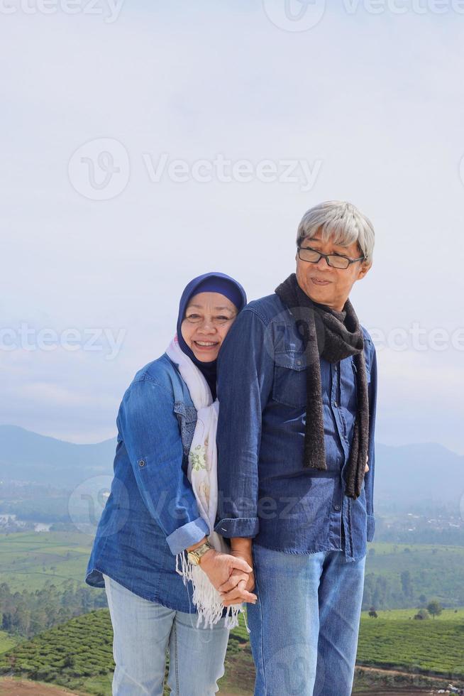 Aziatisch bejaarde echtpaar in casual stijl lacht, oude man knuffelt zijn vrouw en houdt elkaars hand vast voor esthetische koepel en bomen. foto