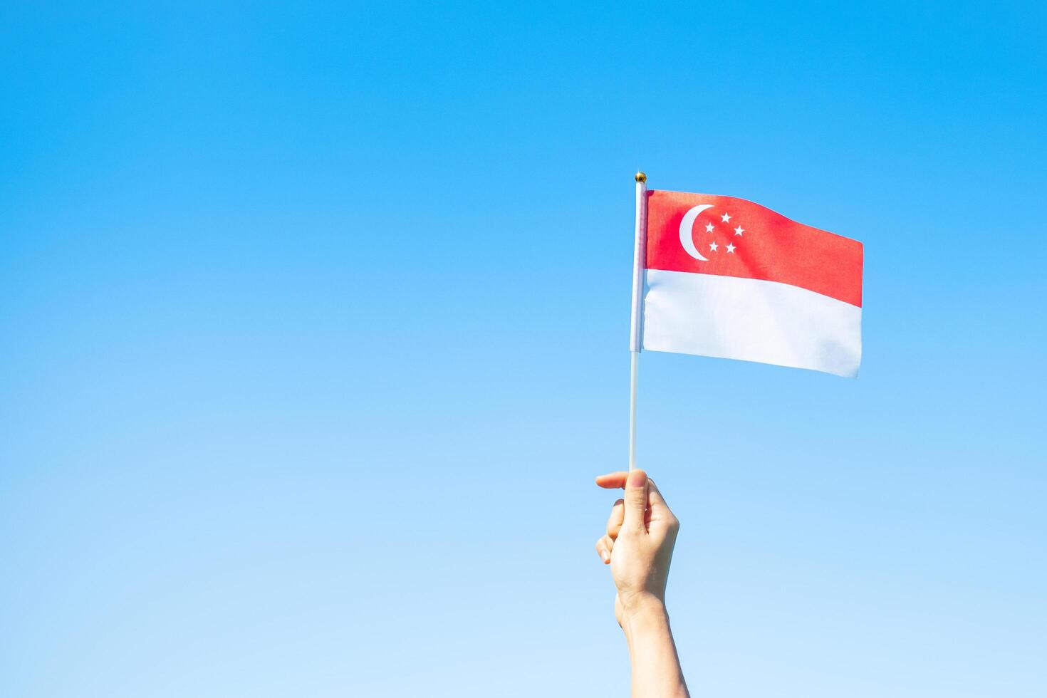 hand met singapore vlag op blauwe hemelachtergrond. Singapore nationale feestdag en gelukkige vieringsconcepten foto