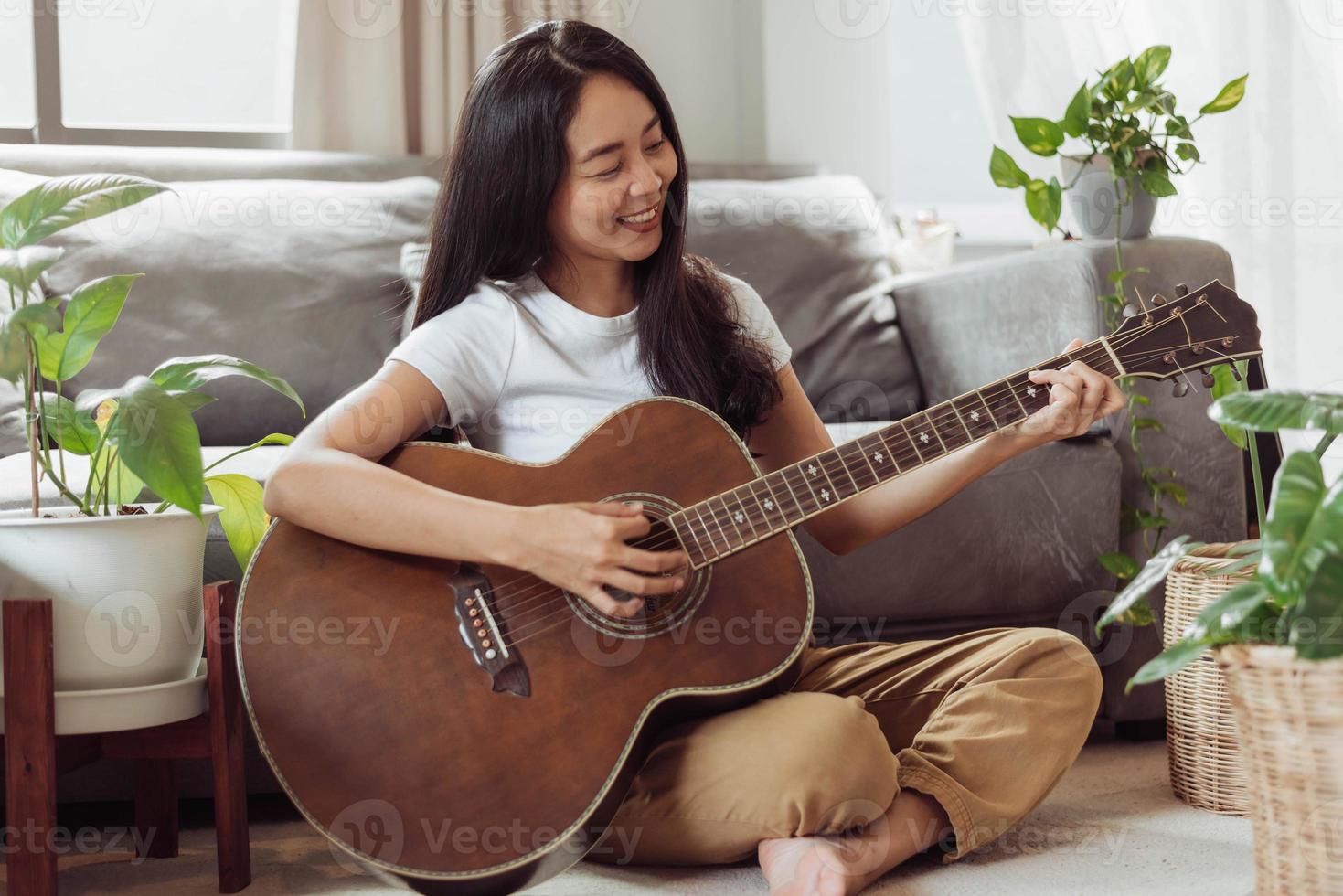 vrouw gitaar spelen thuis. mooie vrouw lacht en speelt gitaar met haar planten in de woonkamer. foto