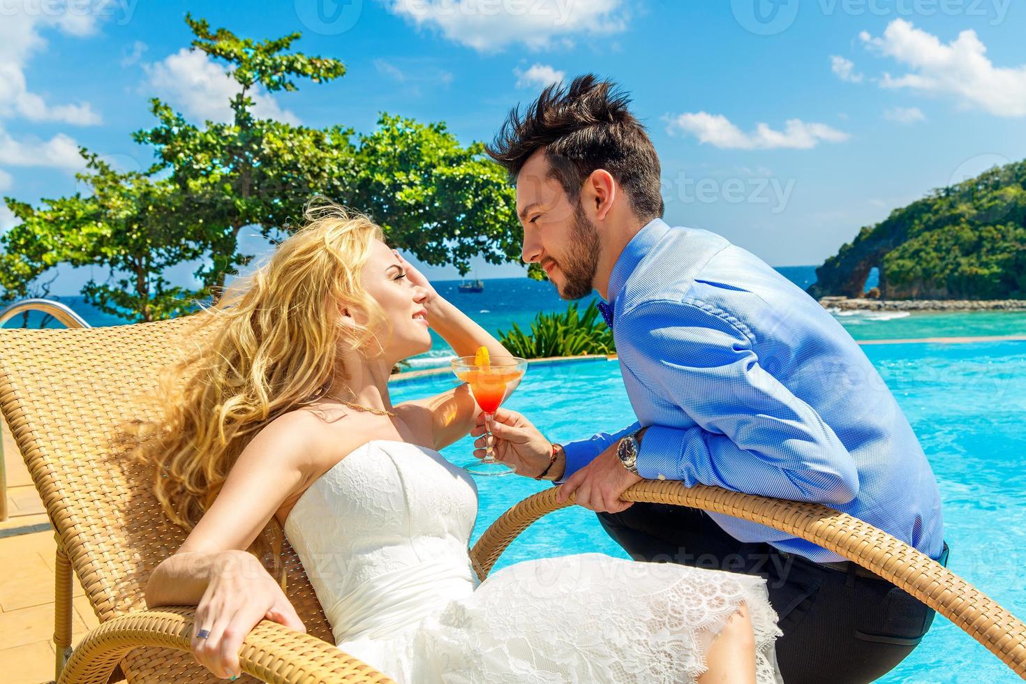 gelukkige bruid en bruidegom genieten van een cocktail oneindigheid bij het zwembad foto