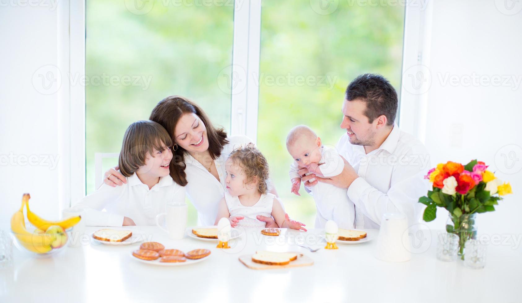 jong gezin met drie kinderen genieten van het ontbijt in de buurt van groot raam foto