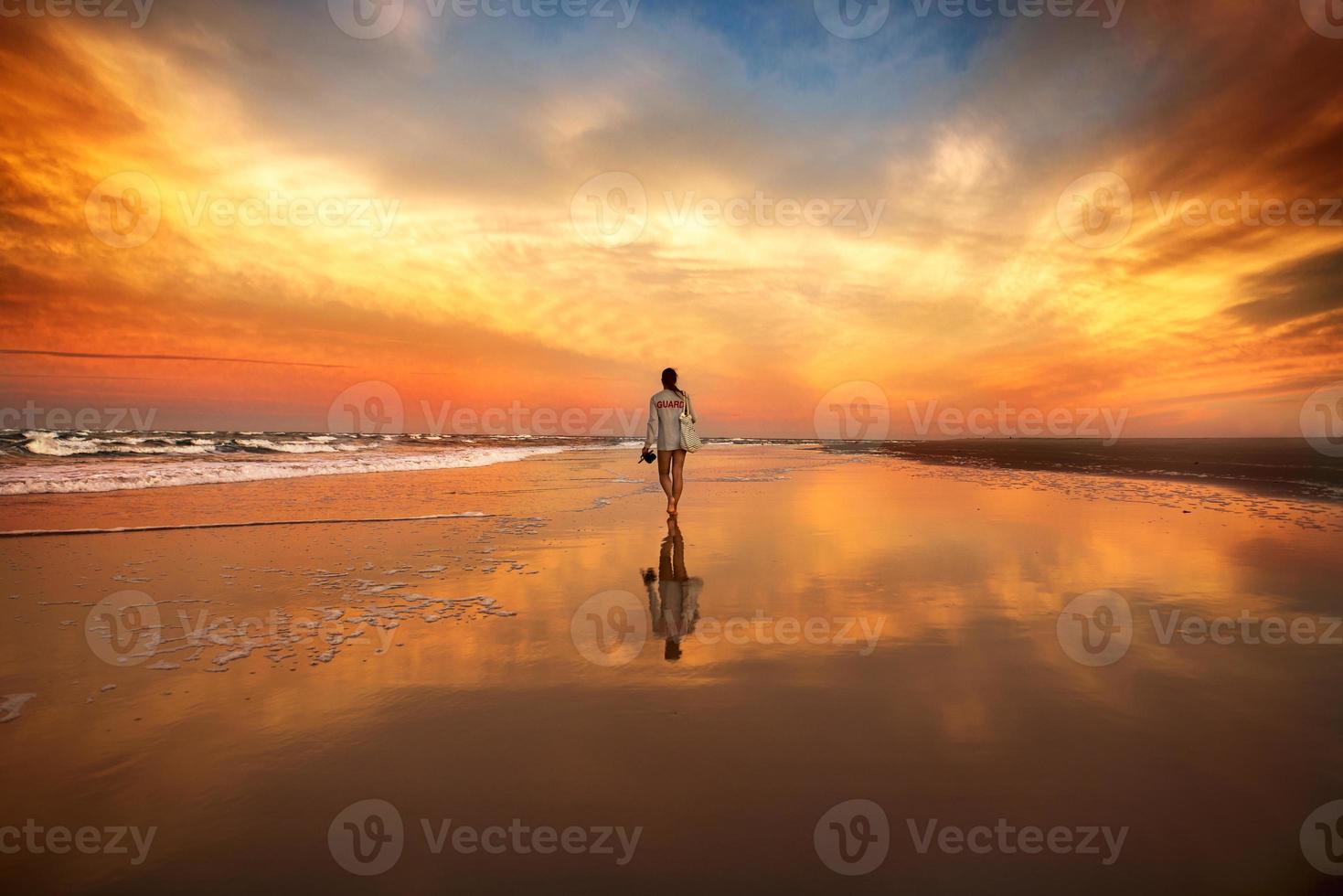 vrouw lopen op het strand in de buurt van de oceaan bij zonsondergang foto
