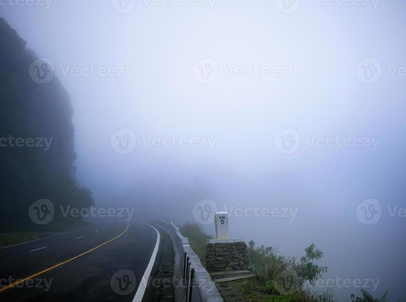 asfaltweg met gele lijn op de top van de berg in de ochtendmist foto