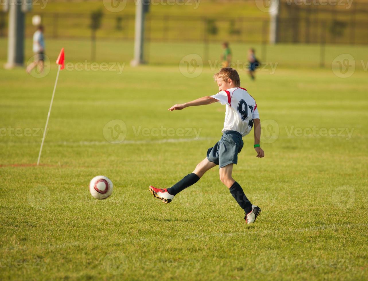 jonge jongen voetballer schopt de bal in het doel foto