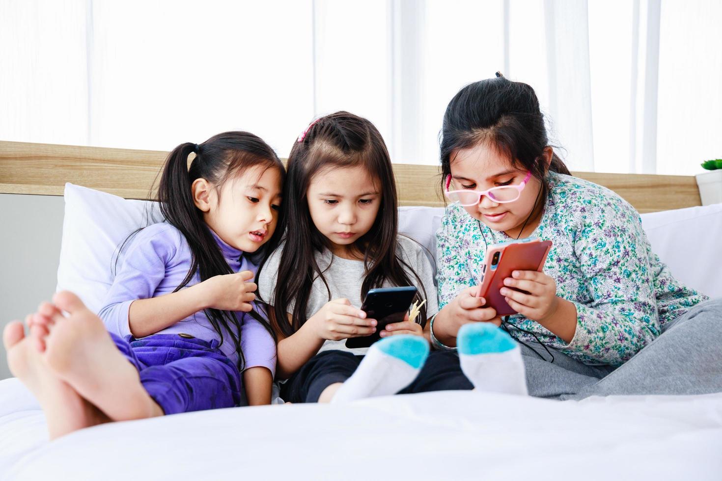 drie kleine meisjes die samen thuis een spel op smartphone spelen foto
