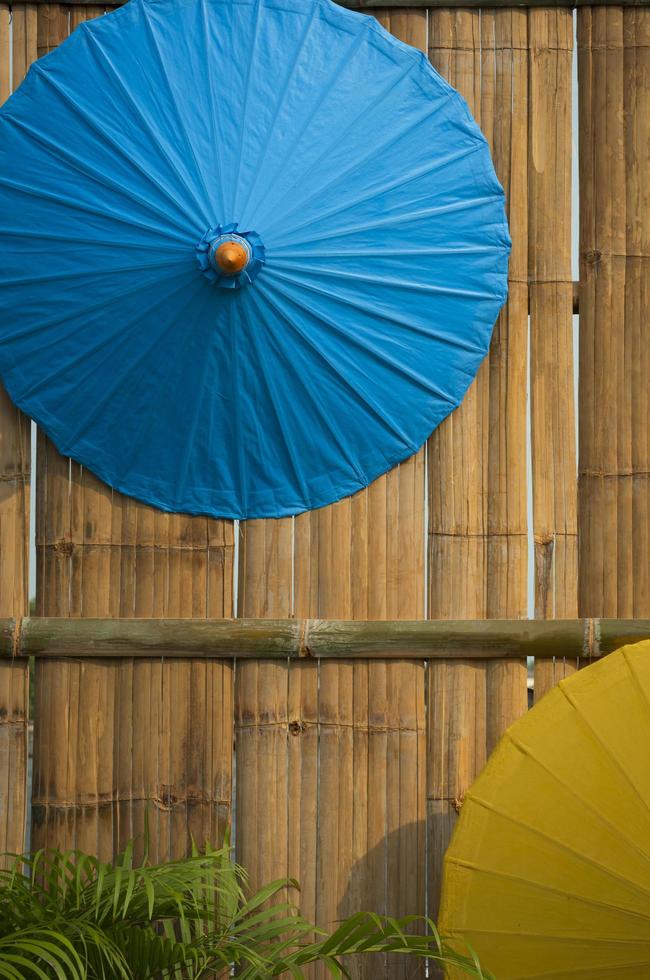 deel van blauwe en gele papieren paraplu's die op bamboe houten muurachtergrond hangen in vintage stijl en verticaal frame foto