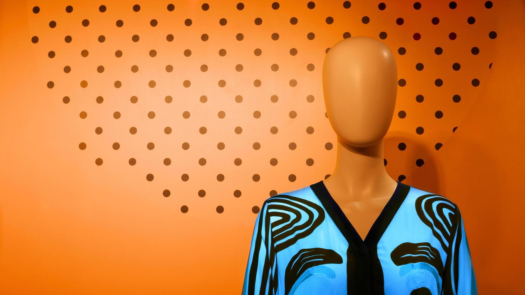 mannequin in een casual blauwe satijnen blouse met lange mouwen op een kleurrijke oranje muurdecoratieachtergrond, close-up met kopieerruimte foto