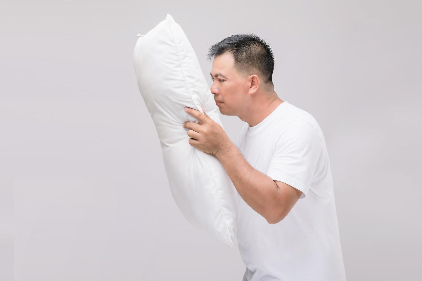 het kussen stinkt. portret aziatische man die wit kussen vasthoudt en een slechte geur krijgt. studio-opname op grijs foto