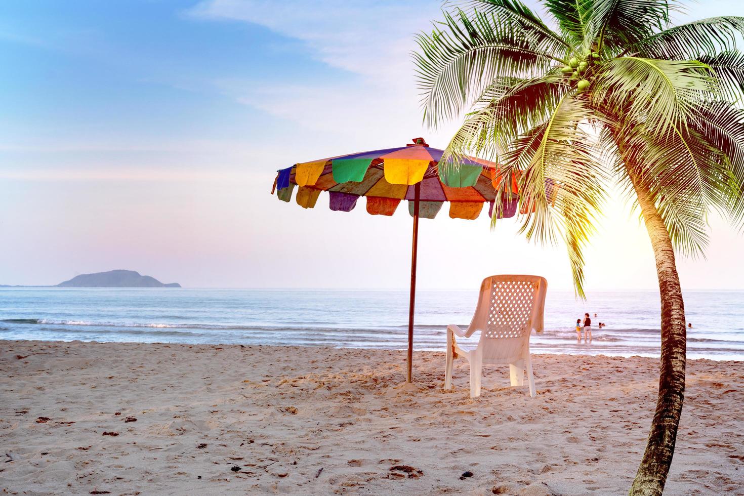 witte strandstoel en parasol op tropisch strand met oranje lucht foto