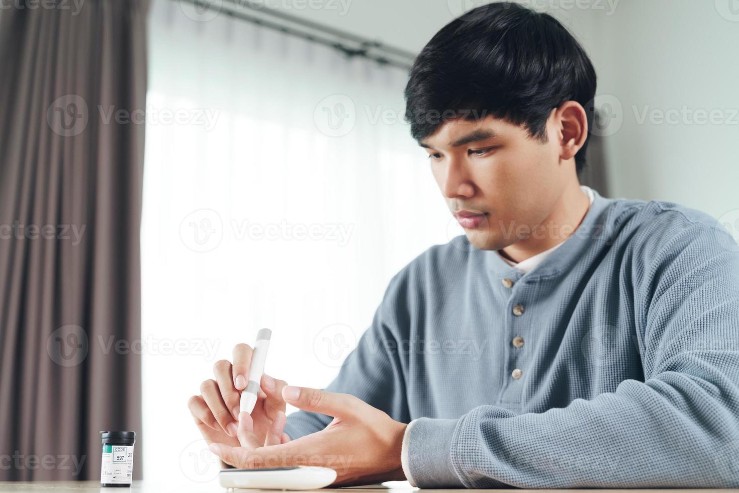 Aziatische man die lancet op vinger gebruikt voor het controleren van de bloedsuikerspiegel door glucosemeter, gezondheidszorg en medisch, diabetes, glycemieconcept foto