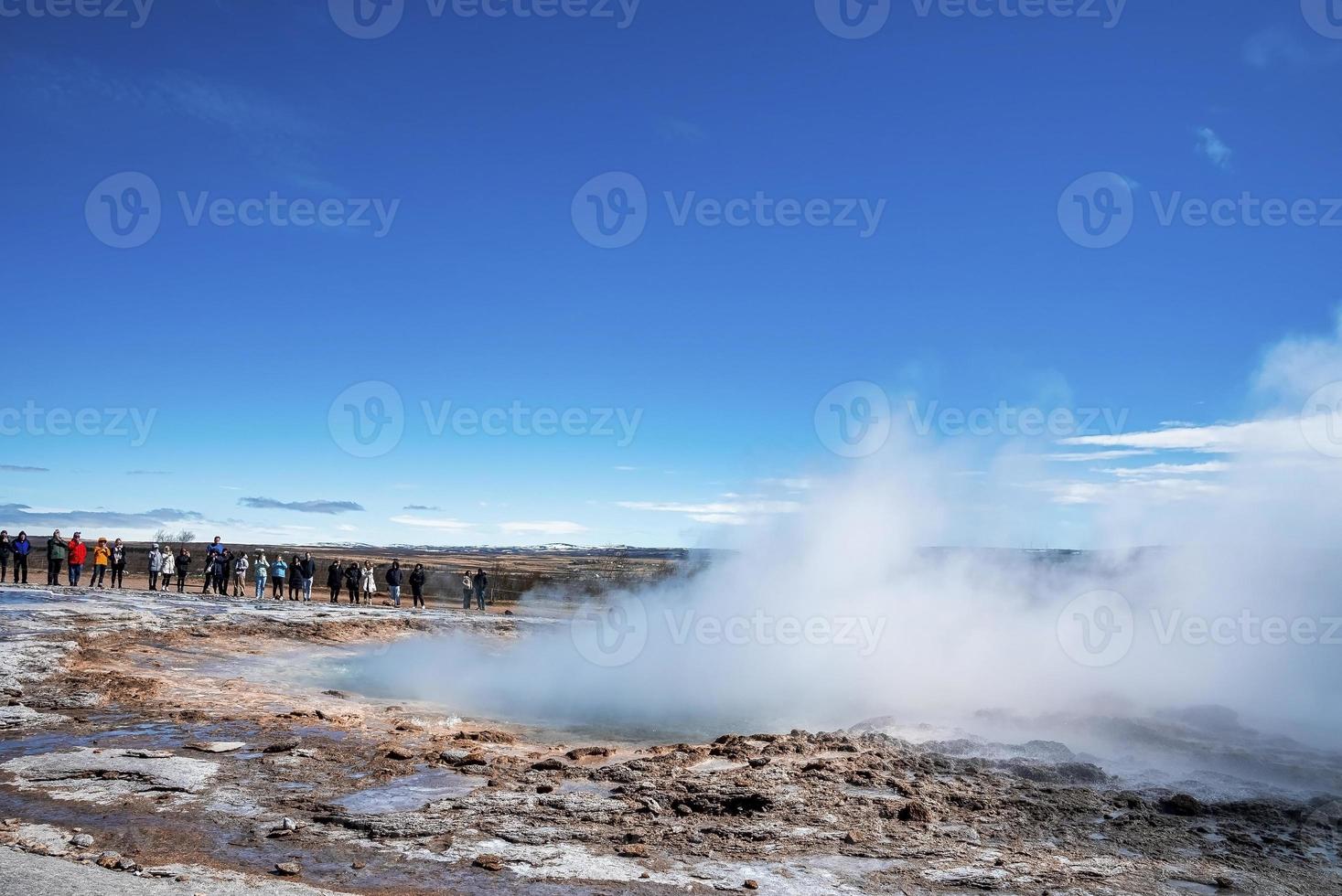 toeristen die de uitbarsting van de Strokkur-geiser in de vallei tegen de blauwe lucht verkennen foto