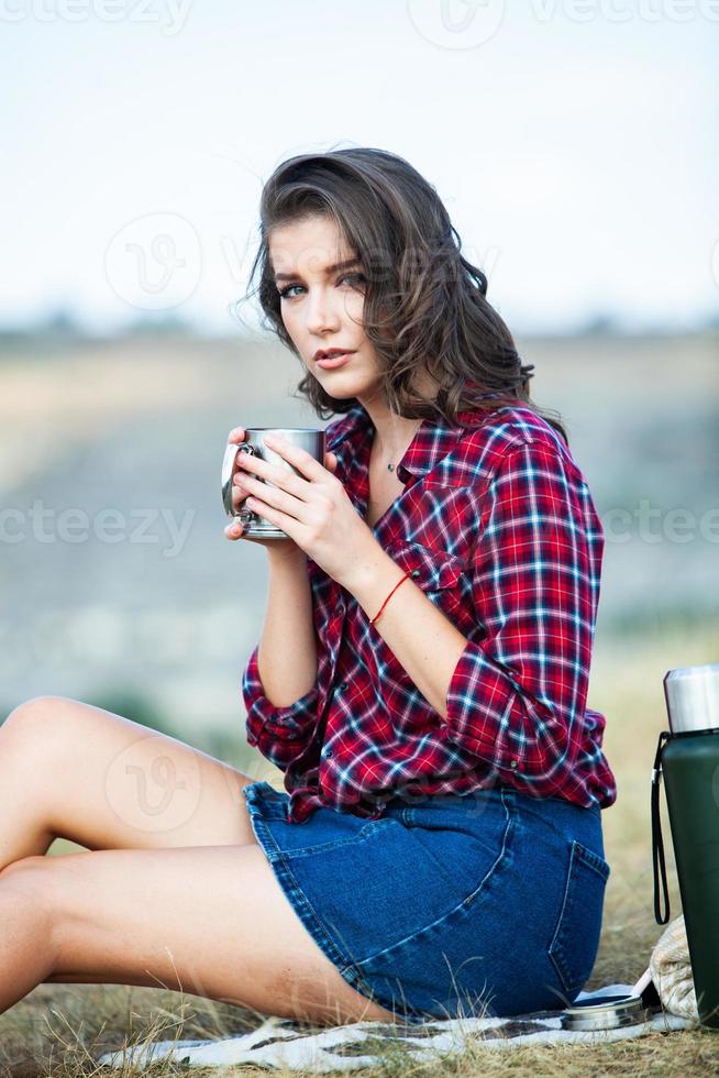 mooie vrouw drinkt thee buitenshuis. hipster vrouw ontspannen in de natuur foto