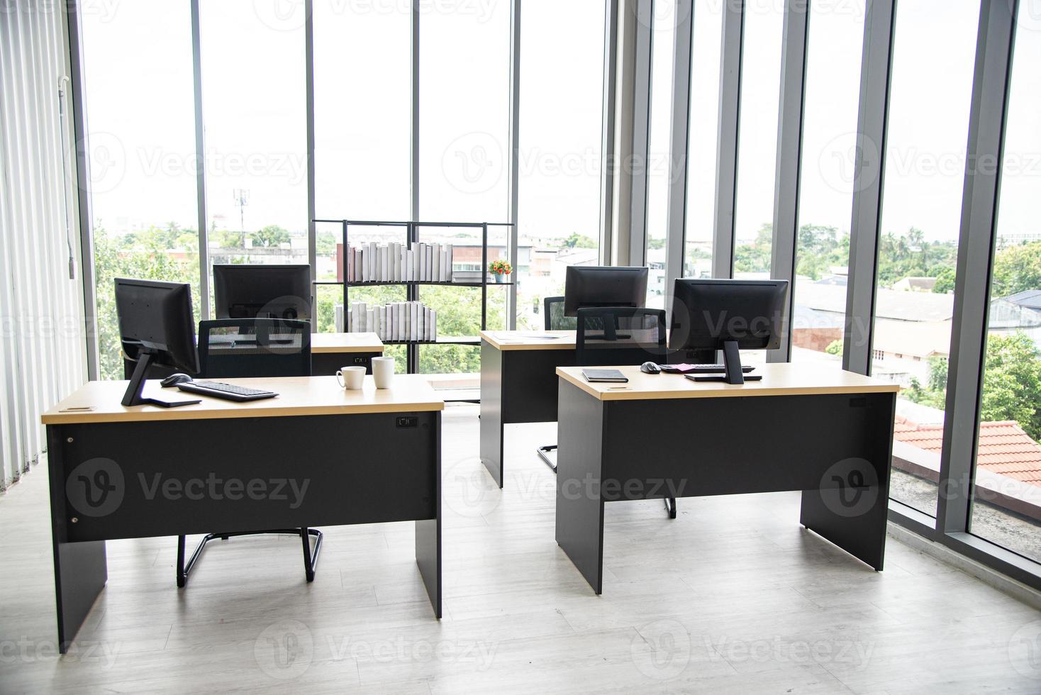 modern kantoorinterieur met tafelcomputermonitor-notebook en groot glazen raam rond de kamer zonder mensen foto
