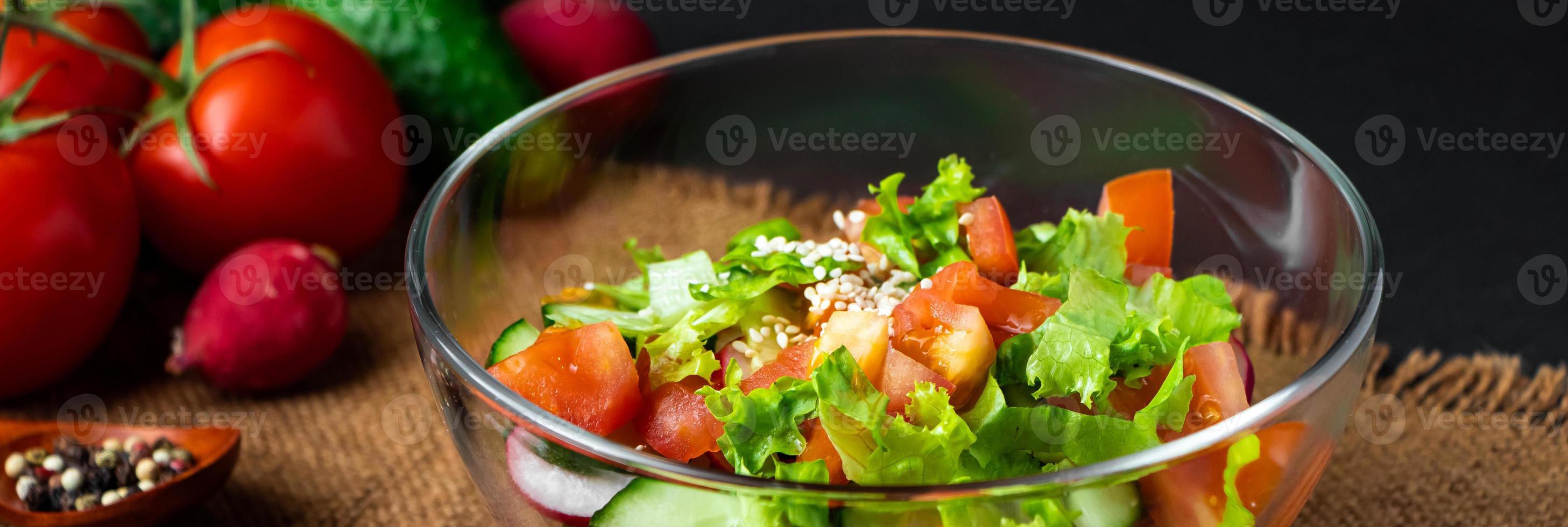 seizoensgebonden zomergroentesalade in een glazen kom op donkere achtergrond. veganistisch biologisch voedsel, dieetmaaltijd in rustieke stijl. foto