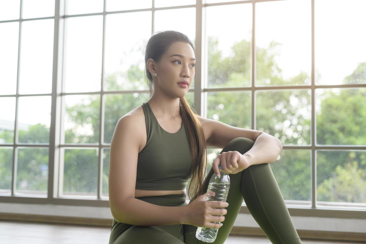 jonge fitness vrouw in sportkleding drinkwater na thuis sporten, gezond en levensstijl. foto