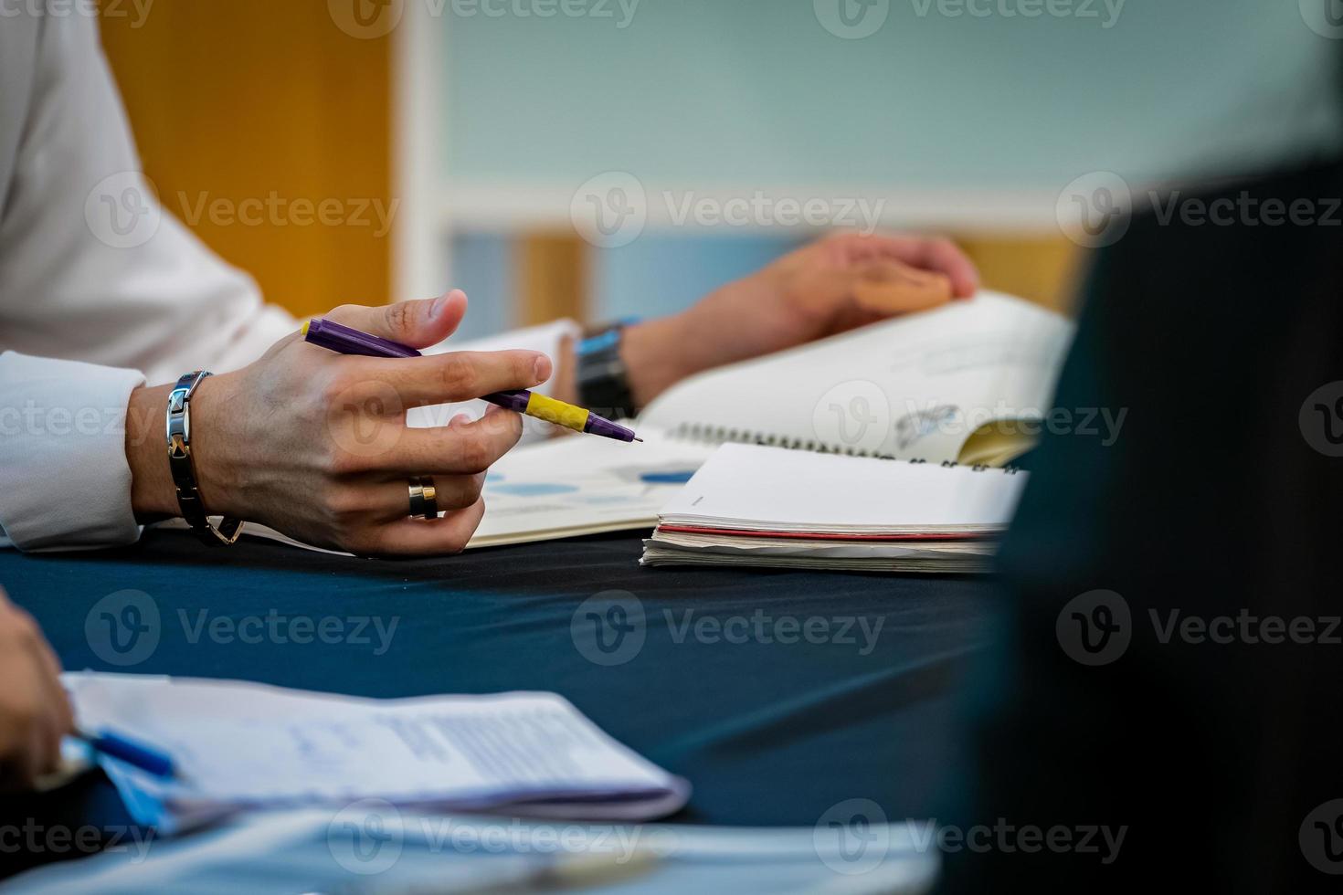 dicht bij de hand van de mens, hij houdt een paarse pen vast en concentreert zich om de docent te luisteren terwijl hij het handboek op tafel opent. foto