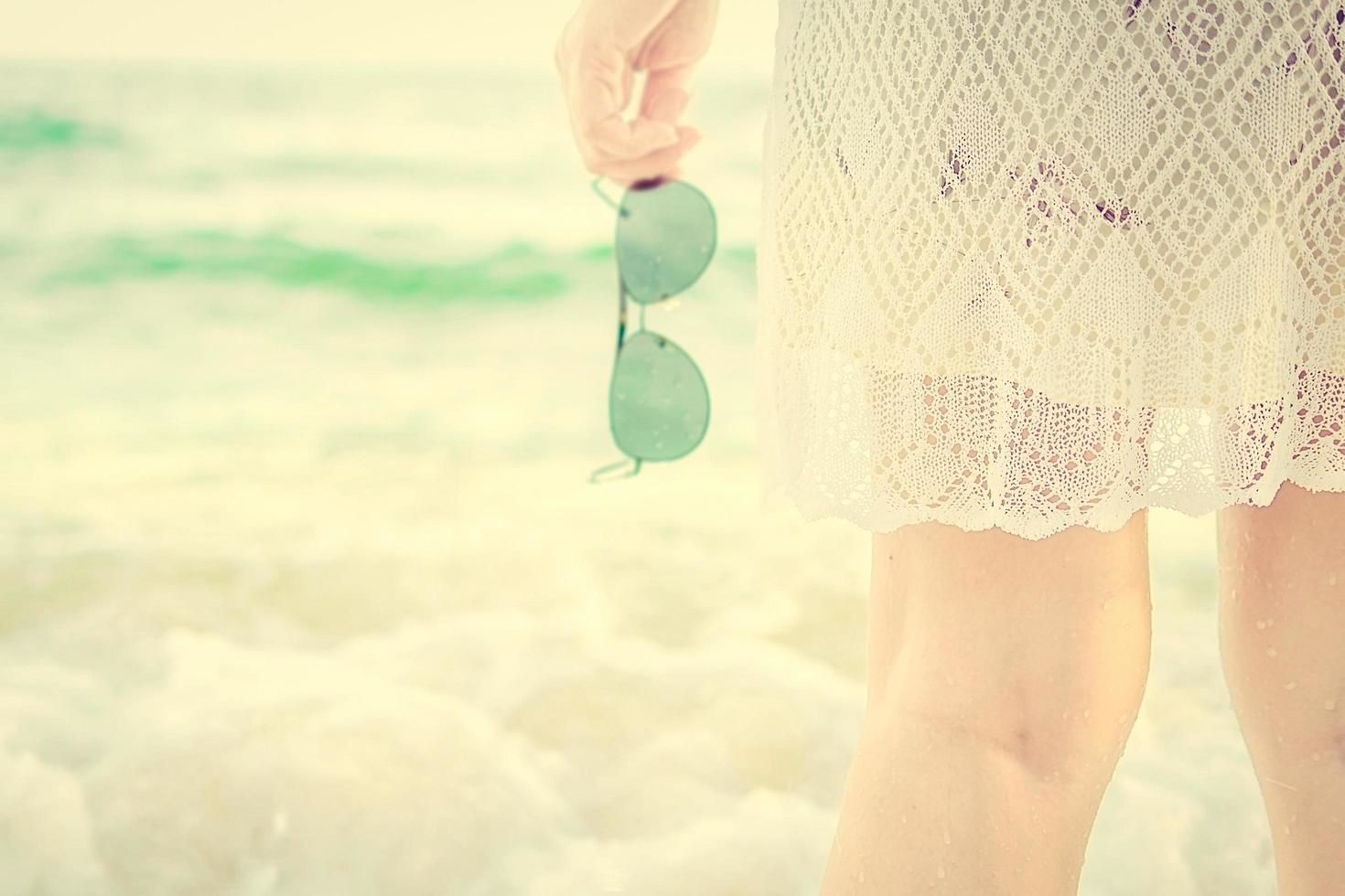 vintage foto van een dame die een zonnebril vasthoudt terwijl ze op een strand staat
