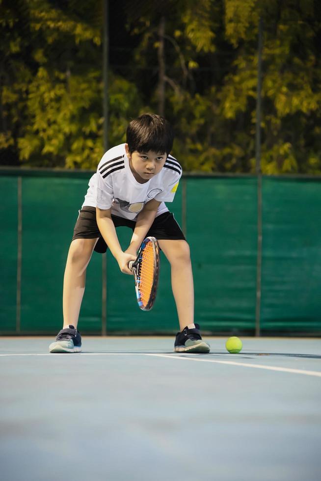 Aziatische jongen die tennisbaan speelt tijdens zijn oefensporttijd - tennissport met mensenconcept foto